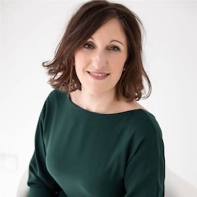 A woman with shoulder-length brown hair and a green top smiles at the camera against a plain white background.