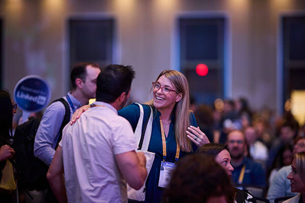 A woman smiling and talking with a man at a crowded Gainsight Pulse event, both wearing name badges and conference lanyards, with other attendees in the background.