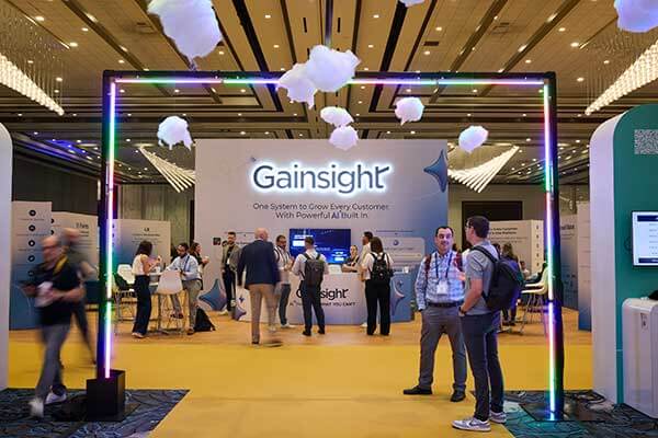 People gather at a Gainsight Pulse conference booth under hanging cloud decorations, with a neon-lit archway in the foreground and display screens and banners in the background.
