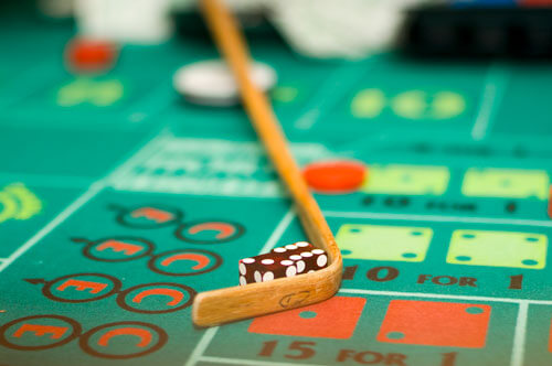A close-up of a craps table at Gainsight Pulse shows a wooden stick moving two dice, with betting chips and numbers visible on the green felt surface in the background.
