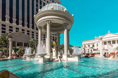A luxurious pool with fountains and a domed, Roman-style pavilion surrounded by columns sets the scene for Gainsight Pulse, with elegant buildings and palm trees in the background under a clear blue sky.